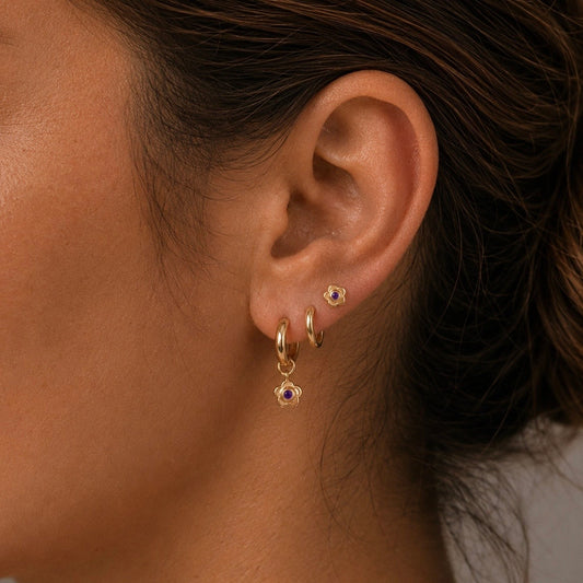 Close-up of an ear wearing 14ct gold vermeil amethyst flower huggie hoop earrings paired with a matching 14ct gold vermeil amethyst flower stud in a three lobe ear stack.