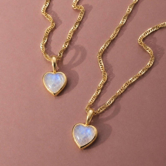Two gold vermeil rainbow moonstone heart pendant necklaces on a muted dusky pink background.