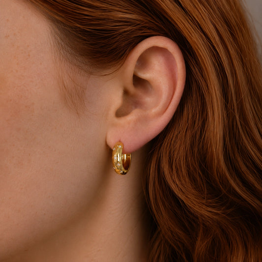 Close-up of a model wearing 14ct gold vermeil huggie hoop earrings with star-set cubic zirconia stones.