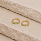 Pair of 14ct gold vermeil huggie hoop earrings with faceted peridot gemstones on a textured beige stone surface, featuring a visible 925 hallmark on the inner band.