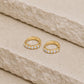 Pair of 14ct gold vermeil rainbow moonstone huggie hoop earrings displayed on a textured beige stone surface, featuring six round rainbow moonstones on each hoop and a 925 stamp on the inner hoops.