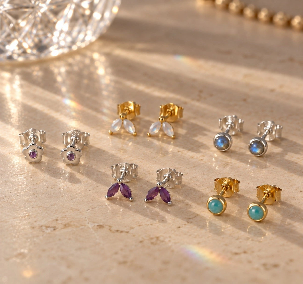 Gold vermeil and sterling silver gemstone stud earrings with moonstone, amethyst, labradorite and amazonite on a warm marble surface.