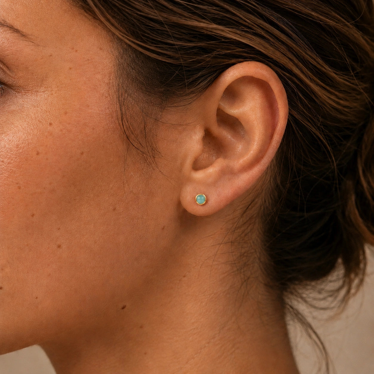 Close-up of a model wearing 14ct gold vermeil amazonite round stud earrings with smooth cabochon stones.