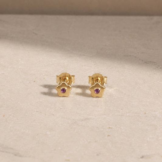 Pair of 14ct gold vermeil flower stud earrings with amethyst centre stones, displayed on a light beige stone surface with 925 butterfly backs visible.