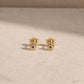 Pair of 14ct gold vermeil flower stud earrings with amethyst centre stones, displayed on a light beige stone surface with 925 butterfly backs visible.