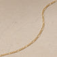 Close up of a 14ct gold vermeil Figaro chain necklace laid on a light beige stone background, showing the elongated and round link pattern.