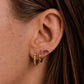 Close up of a model wearing 14ct gold vermeil faceted peridot huggie earrings and amethyst marquise stud earrings, shown on the ear with natural skin texture and brown hair tucked behind the ear.