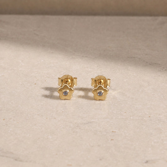 Pair of 14ct gold vermeil flower stud earrings with rainbow moonstone centre stones, displayed on a light beige stone surface with 925 butterfly backs visible.