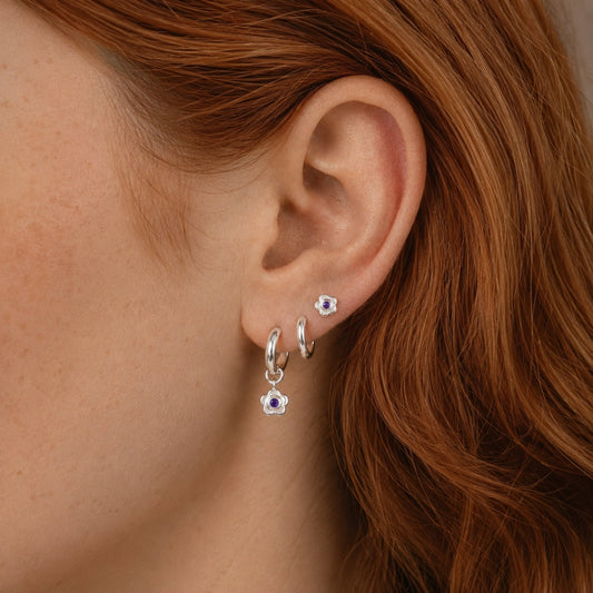 Close-up of an ear wearing sterling silver amethyst flower huggie hoop earrings with a matching sterling silver amethyst flower stud in a three lobe ear stack.