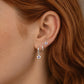 Close-up of an ear wearing sterling silver amethyst flower huggie hoop earrings with a matching sterling silver amethyst flower stud in a three lobe ear stack.