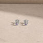 Pair of sterling silver flower stud earrings with amethyst centre stones, displayed on a light beige stone surface with 925 butterfly backs visible.