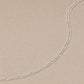 Close-up of a sterling silver Figaro chain necklace with alternating long and short links on a neutral beige stone background.