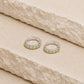 Sterling silver peridot huggie hoop earrings with five light green gemstones on each hoop, displayed on a textured cream stone surface with visible 925 hallmark inside each earring.