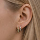 Close-up of a model wearing sterling silver peridot huggie hoop earrings with six light green faceted peridot stones, paired with a polished sterling silver huggie hoop in a minimalist double lobe ear stack.