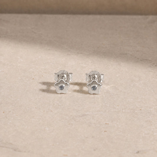 Pair of sterling silver flower stud earrings with rainbow moonstone centre stones, displayed on a light beige stone surface with 925 butterfly backs visible.