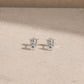 Pair of sterling silver flower stud earrings with rainbow moonstone centre stones, displayed on a light beige stone surface with 925 butterfly backs visible.