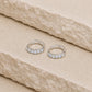 Sterling silver rainbow moonstone huggie hoop earrings with five light blue gemstones on each hoop, displayed on a textured cream stone surface with visible 925 hallmark inside each earring.