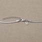 Close-up of a sterling silver snake chain necklace with lobster clasp, extender chain and branded charm tag on a neutral stone background.