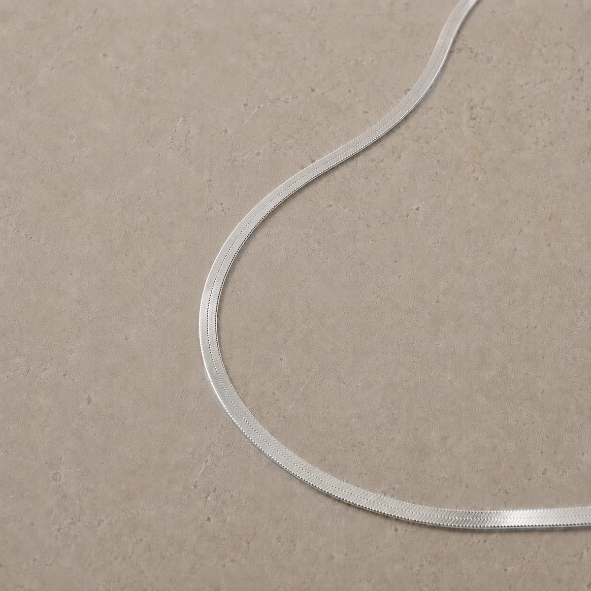 Sterling silver snake chain necklace displayed on a neutral stone background.