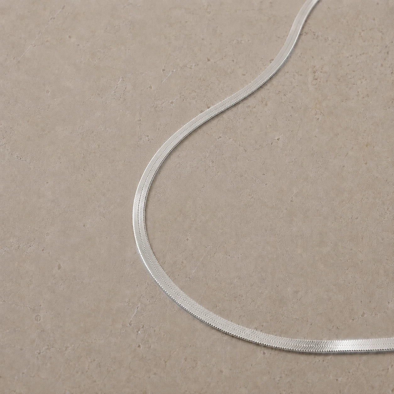 Sterling silver snake chain necklace displayed on a neutral stone background.